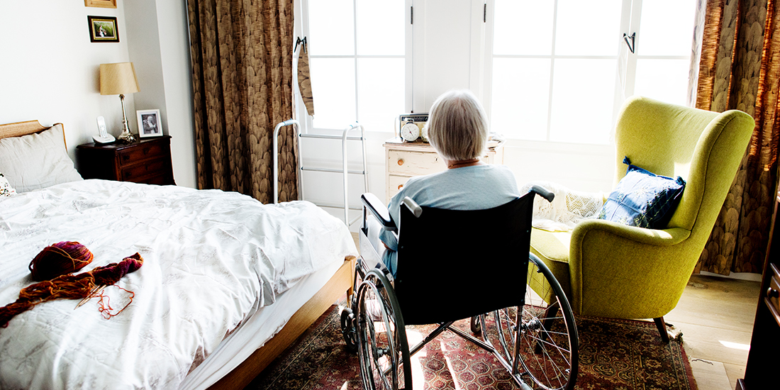 Seniorin im Rollstuhl sitzt in einem freundlich, hellen Zimmer und schaut in Richtung Fenster Seniorin im Rollstuhl sitzt in einem freundlich, hellen Zimmer und schaut in Richtung Fenster